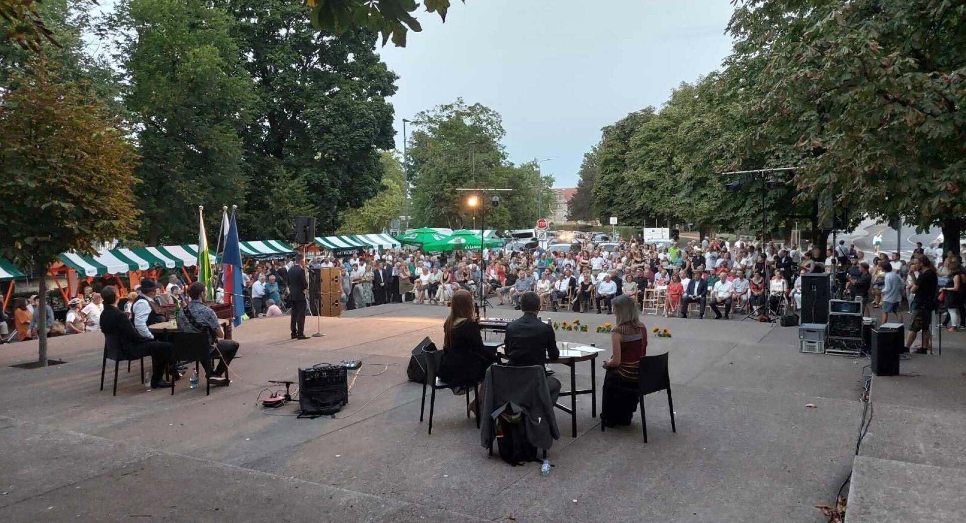 Mnozica obiskovalcev spremlja dogajanje na odru na prostem v parku.