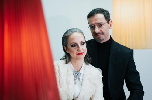 Portret prikazuje žensko s sivimi lasmi, izrazito ličili in v elegantnem belem suknjiču z broško ter moškega z očali in v črnem sakoju, ki stoji za njo, medtem ko je v levem ospredju zamegljen rdeč element.