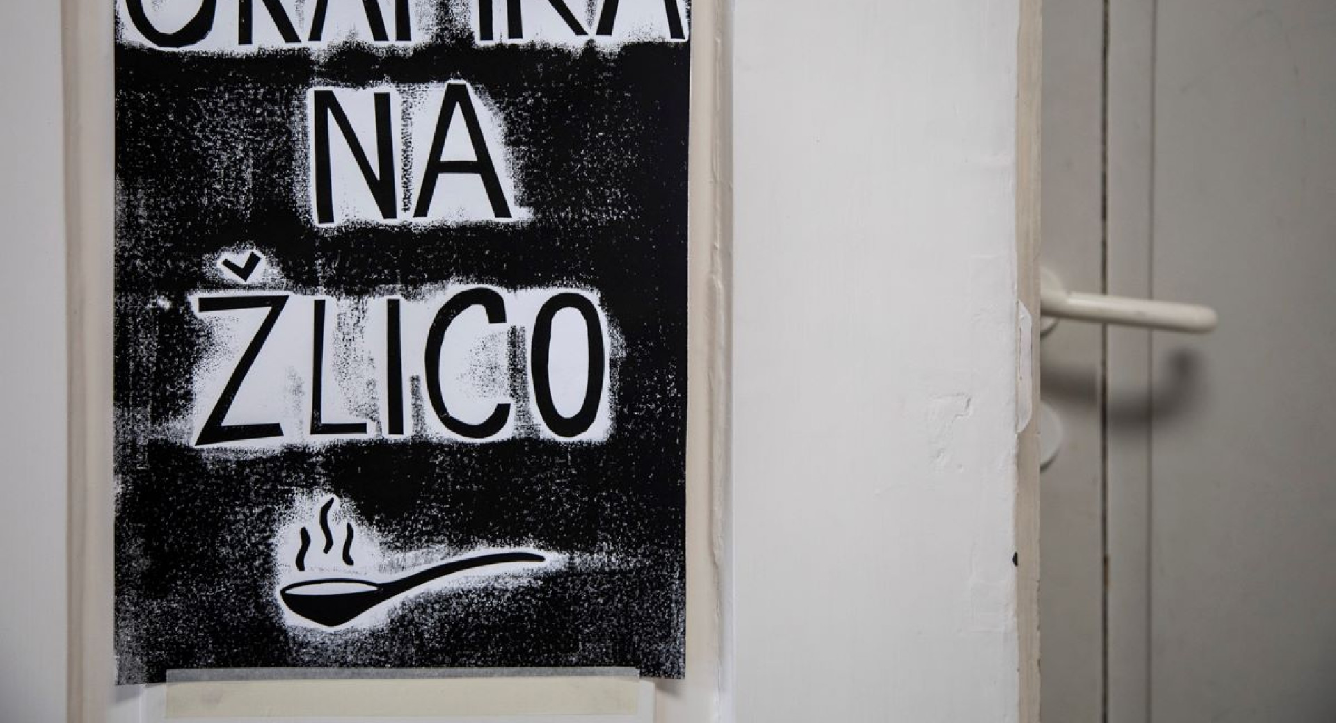 A white door, next to it a black poster displaying a spoon.