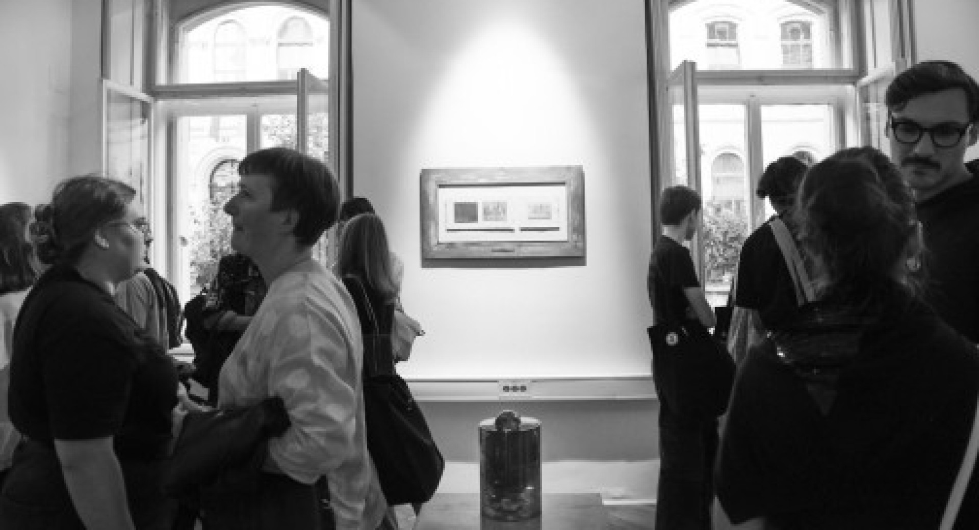 A black-and-white photograph of the interior, where the exhibition is taking place and people are viewing it.