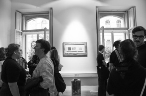 A black-and-white photograph of the interior, where the exhibition is taking place and people are viewing it.