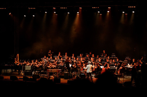 Orkester na odru, obsijan z rdeco svetlobo v objemu teme.