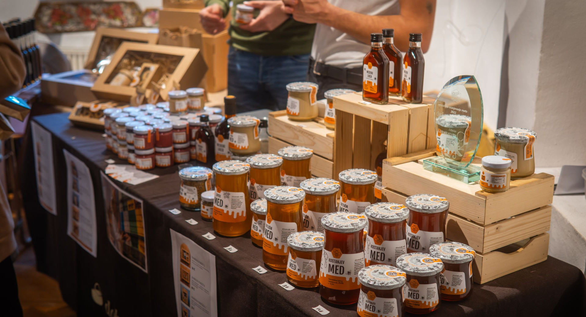 Med in drugi medeni izdelki so razstavljeni na mizi s crnim prtom.