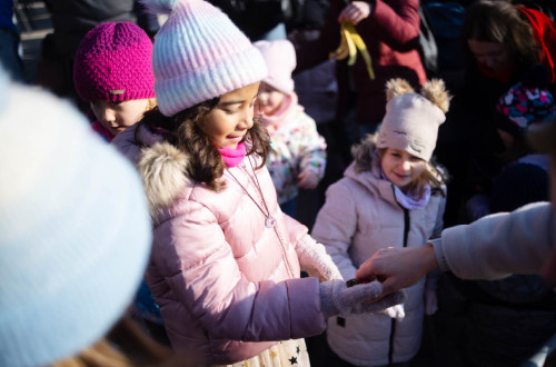 Mlada punca v roza bundi, kapi in rokavicah prejema darilo, v ozadju pa je se vec otrok.