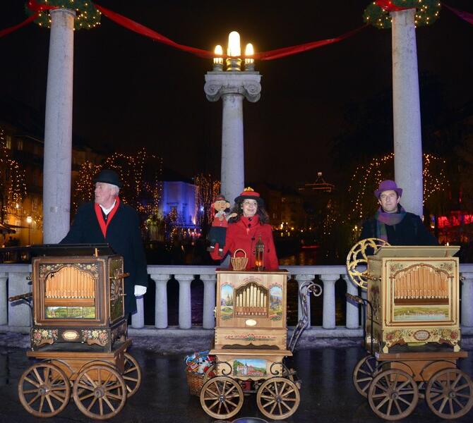 Three buskers in warm clothing with festive lights in the background.