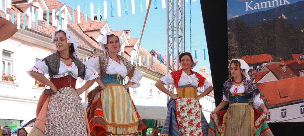 Sul palcoscenico, quattro donne danzano in costumi sloveni tradizionali decorati con motivi colorati.