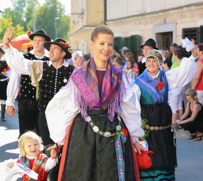 Živahna parada na ulici, kjer so ženske in otroci oblečeni v tradicionalne narodne noše.