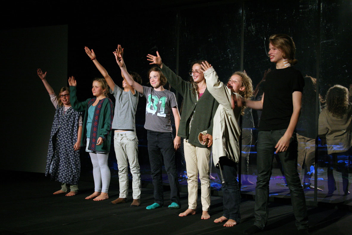 The performers on stage are standing in a line with their right arms raised in the air.