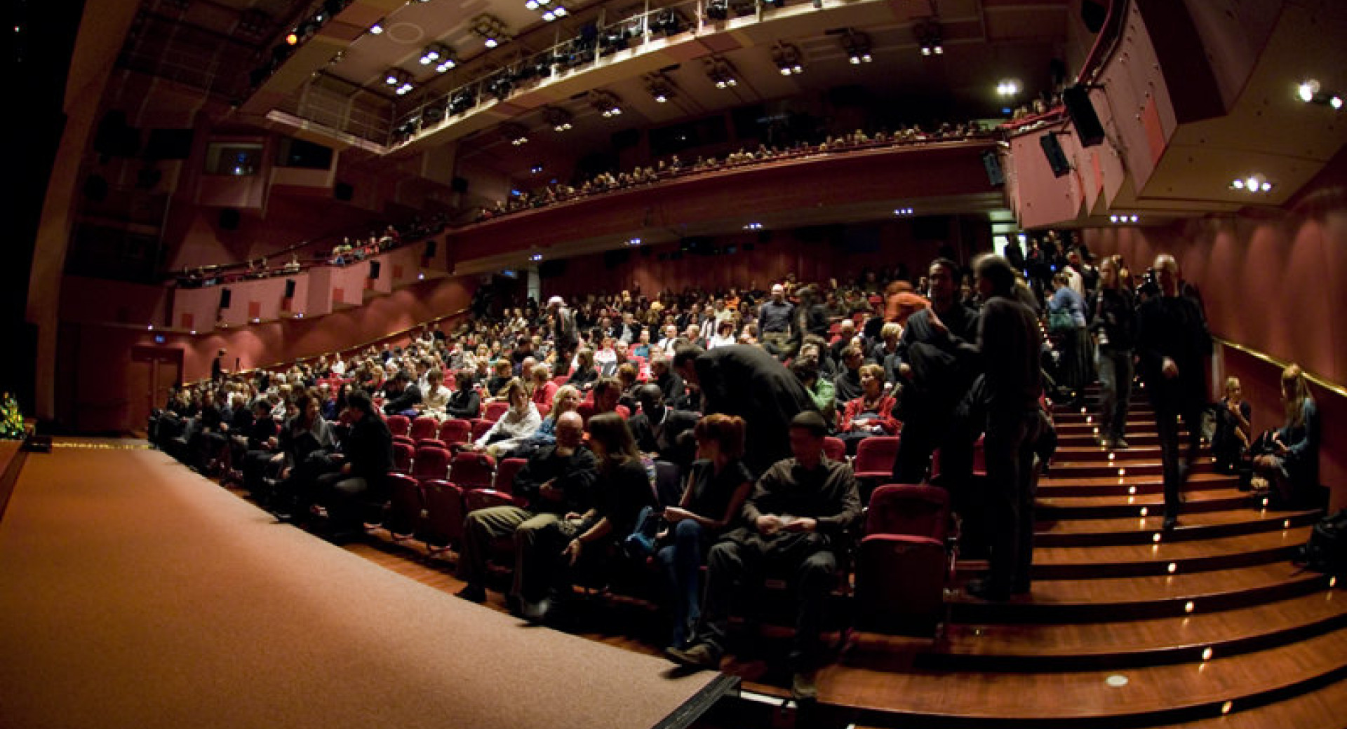 Občinstvo sedi v polni dvorani.
