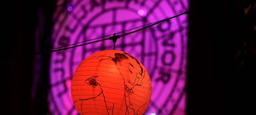 Rdeca papirnata svetilka z umetnisko ilustracijo visi na vrvici pred ozadjem z vijolicnimi odtenki. 