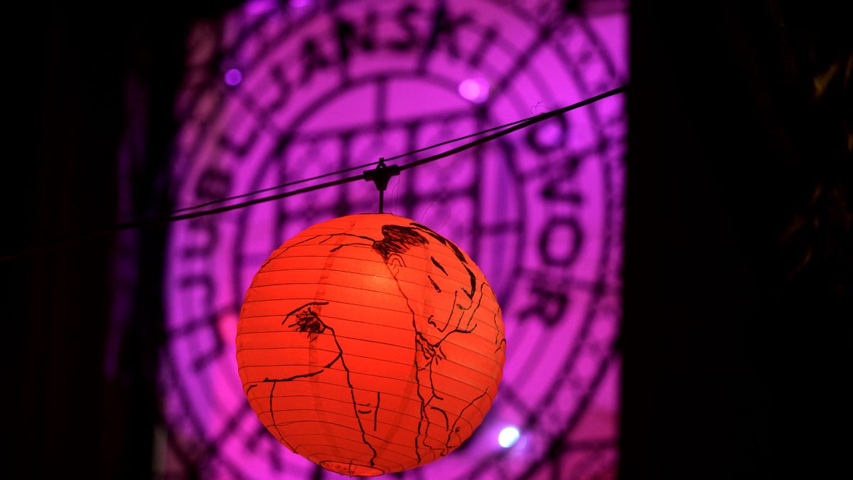 Rdeca papirnata svetilka z umetnisko ilustracijo visi na vrvici pred ozadjem z vijolicnimi odtenki. 