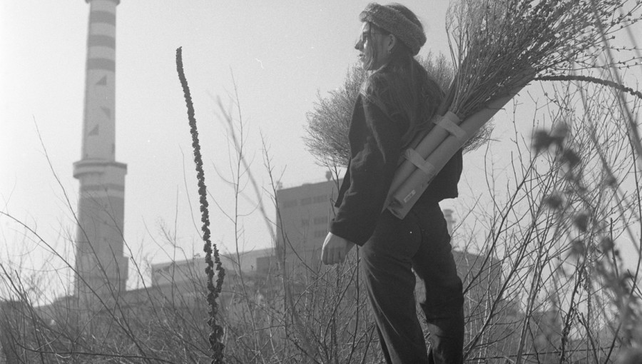 A black-and-white photograph of a woman standing on top of a hill, gazing at the city.