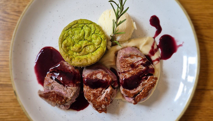 Bel kroznik s tremi okroglimi rezinami mesa in zeleno okroglo rezino zelenjave.