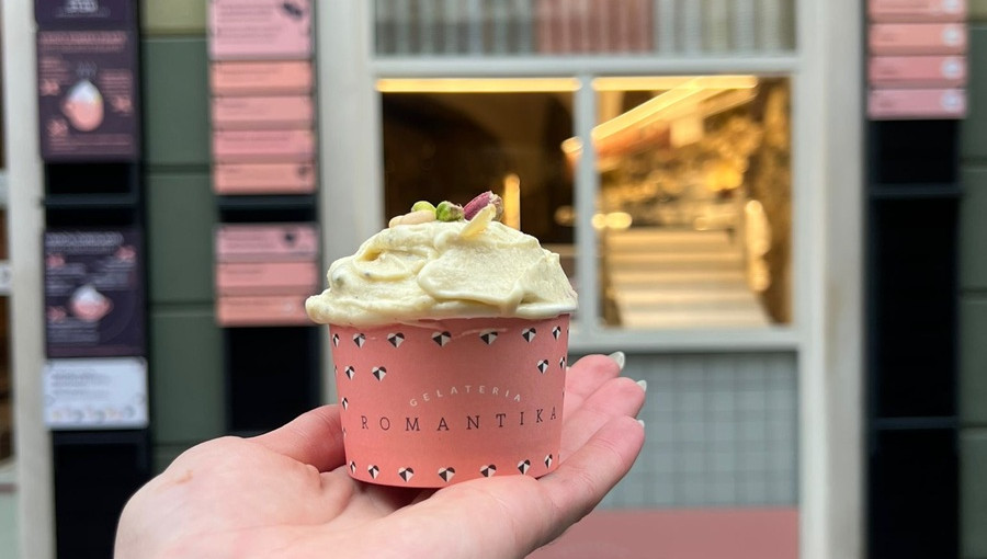 Rumenkast krem sladoled z orescki na vrhu v roza loncku v roki.