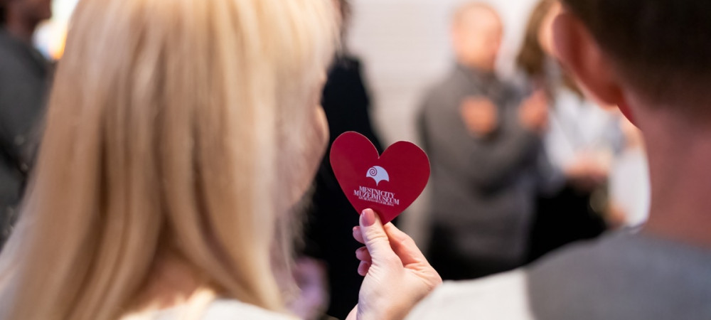 Moski in zenska, ki v rokah drzi majhen rdec srcek, fotografirana od zadaj.