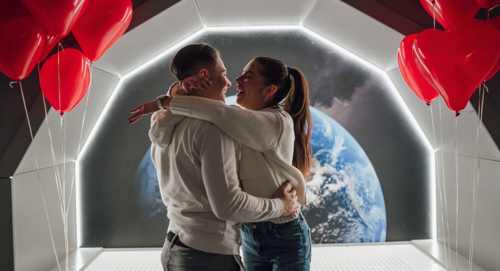 Nasmejan par se objema v futuristični sobi, ki spominja na vesoljsko ladjo