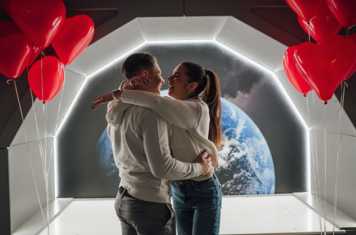 Nasmejan par se objema v futuristični sobi, ki spominja na vesoljsko ladjo