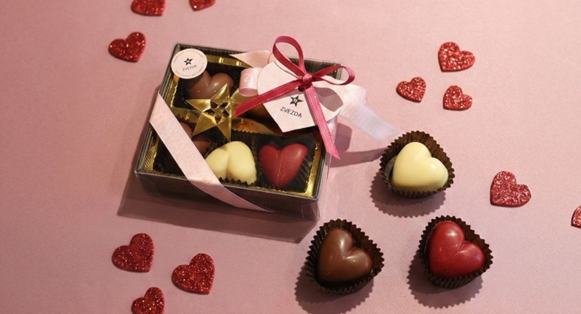 A box of heart-shaped pralines on a pink background.