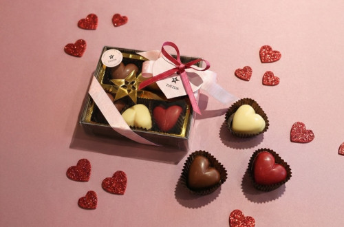 A box of heart-shaped pralines on a pink background.