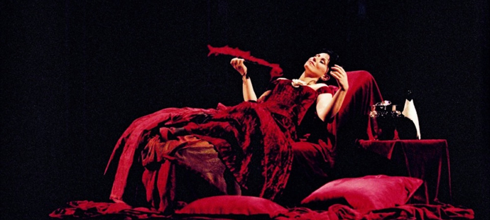 A woman in a long red dress, lying on stage.