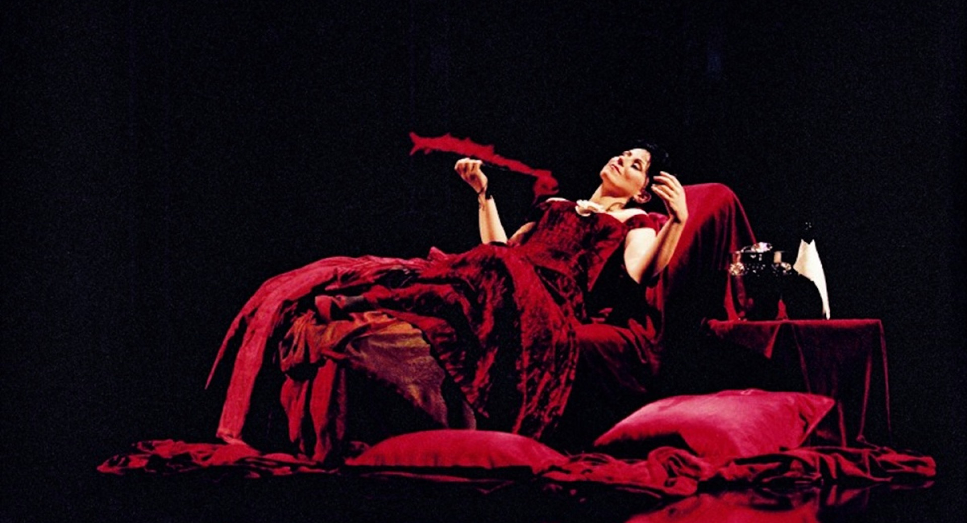 A woman in a long red dress, lying on stage.