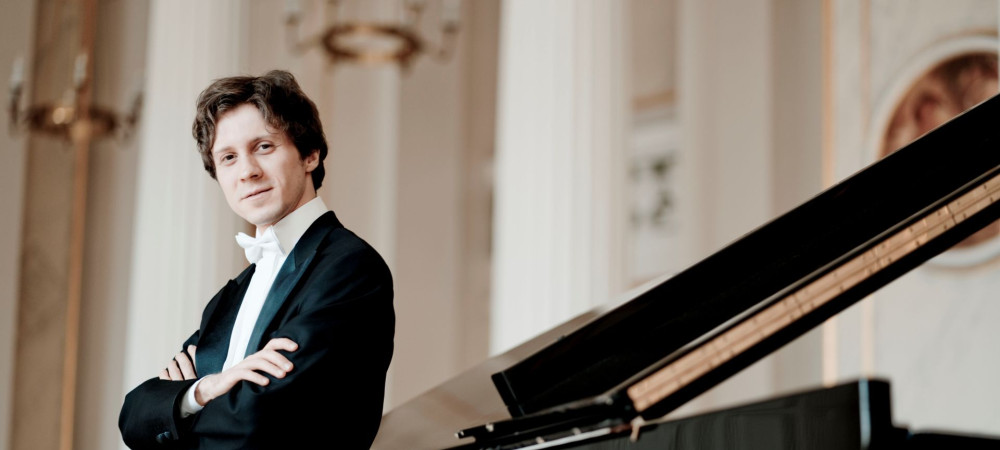 Pianist v obleki se naslanja na klavir.