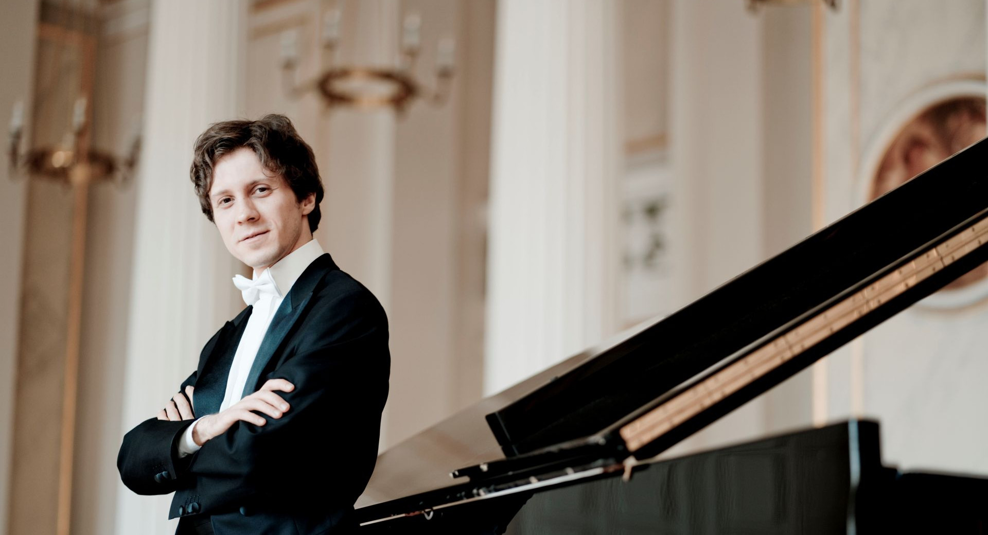 Pianist v obleki se naslanja na klavir.