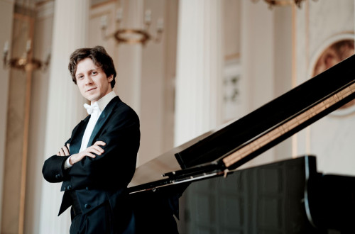 Pianist v obleki se naslanja na klavir.