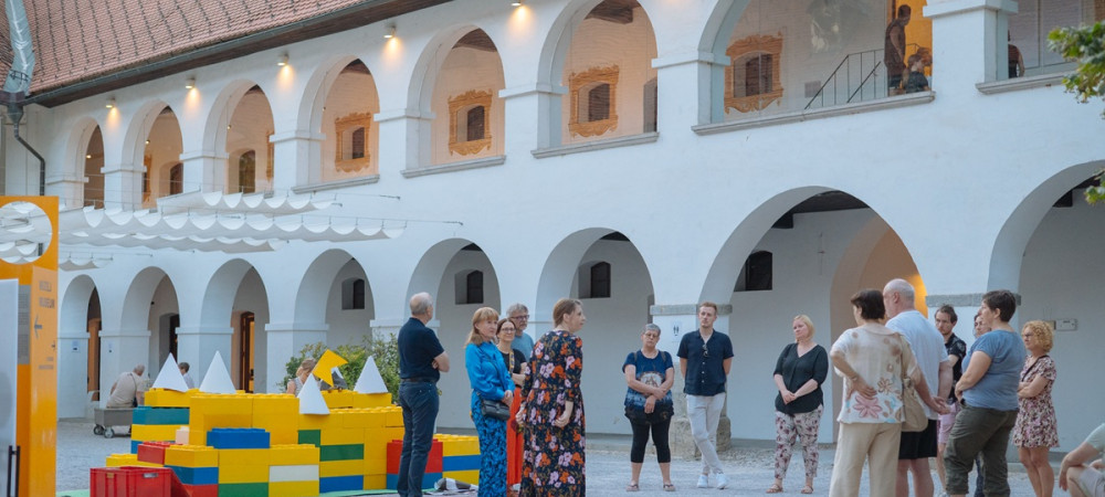 Skupina obiskovalcev na dvoriscu bele stavbe z veliko oboki.