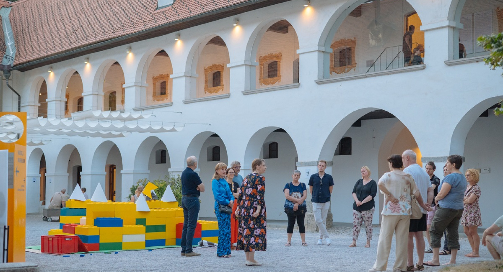 Skupina obiskovalcev na dvoriscu bele stavbe z veliko oboki.