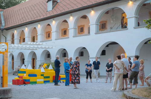 Skupina obiskovalcev na dvoriscu bele stavbe z veliko oboki.