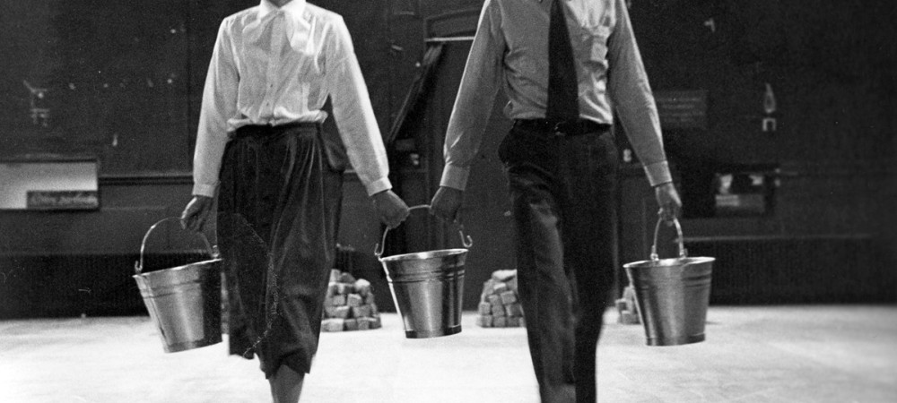 A black-and-white photograph of a man and a woman holding silver buckets in their hands.