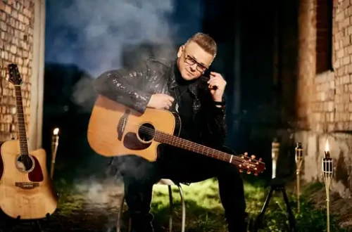 Moski s kitaro sedi na stolu med grajskimi zidovi.