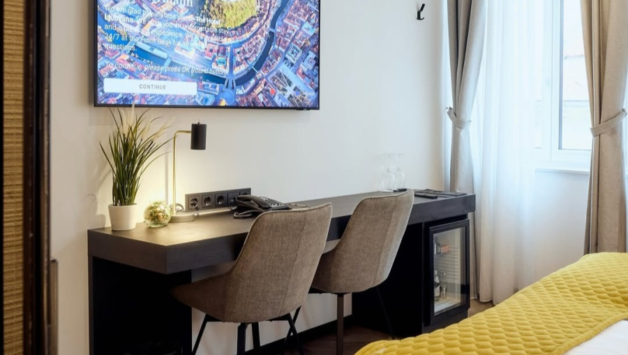 Hotelska soba z rumeno prevleko, televizorjem in dvema stoloma za mizo.