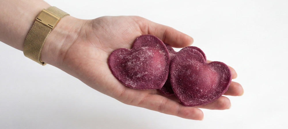 Bližnji posnetek dlani, ki drži dva raviola v obliki srca.