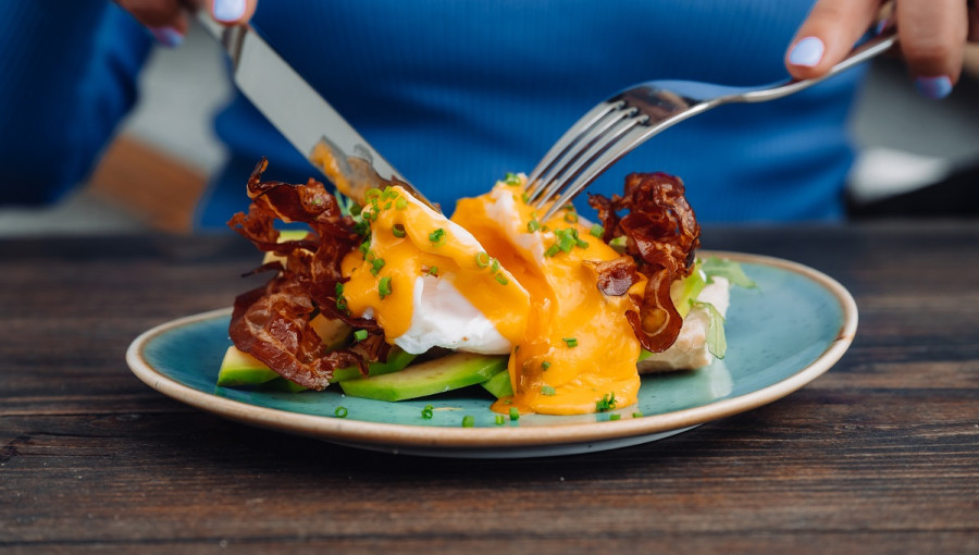 Avocado with baked bacon and egg on a plate.