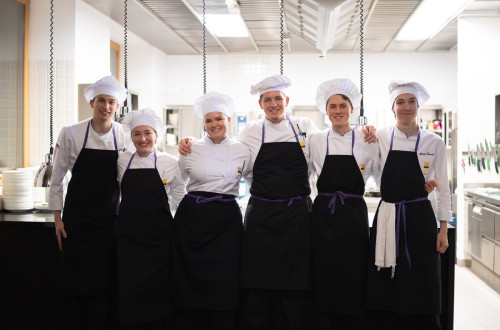 Chefi v belih uniformah s crnimi predpasniki v vrsti.