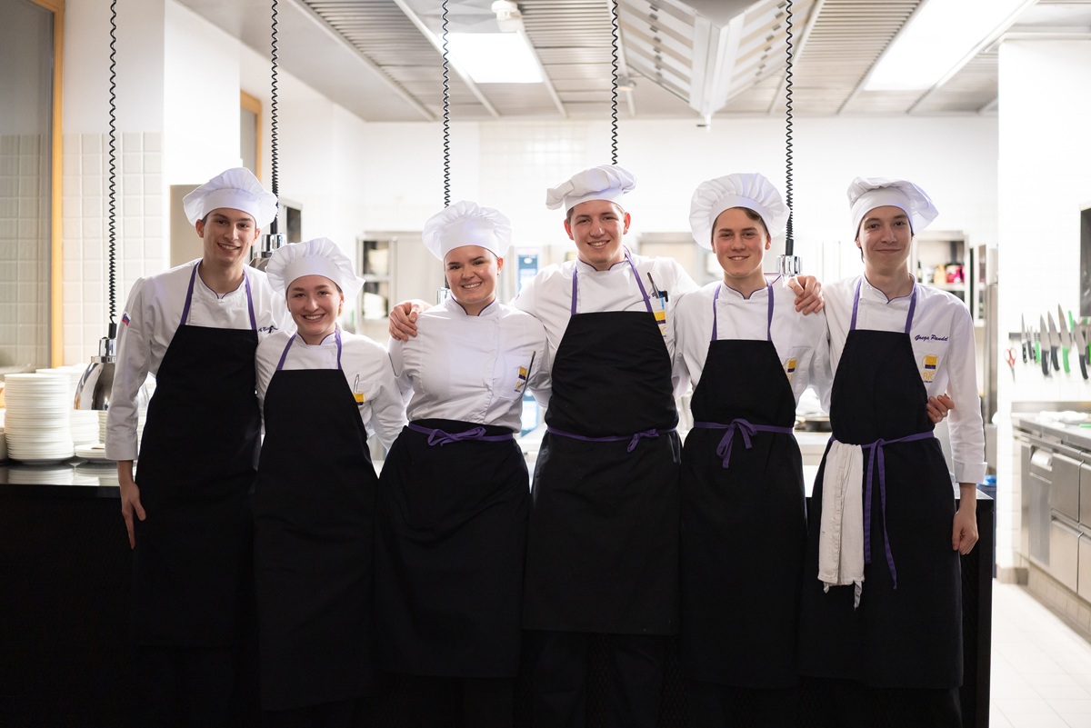 Chefi v belih uniformah s crnimi predpasniki v vrsti.