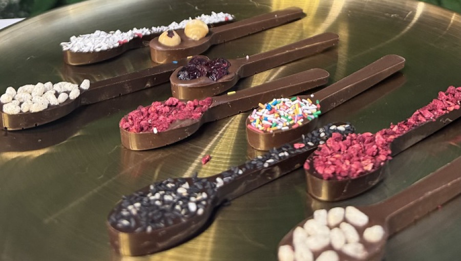 Spoons with various chocolate sprinkles on a golden tray.