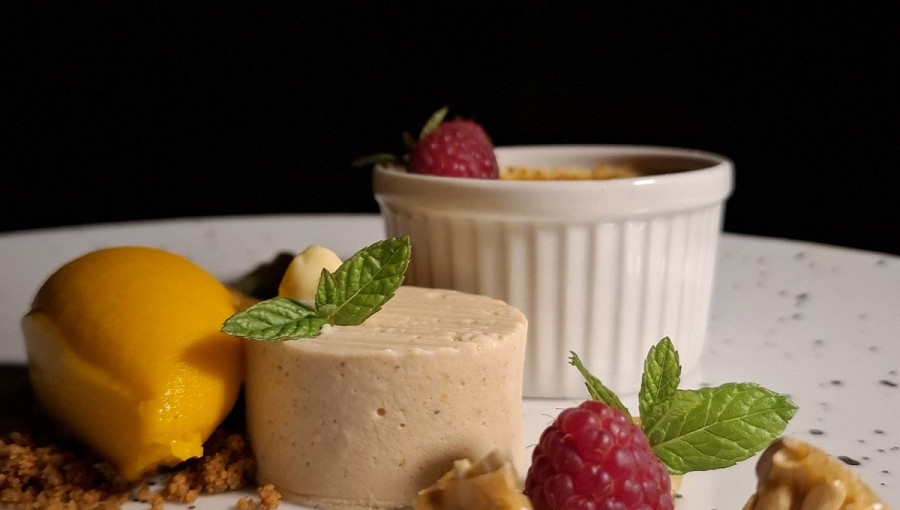 Crno ozadje z belim kroznikom, oblozenim z bucnim sladoledom, strjenko in malinami.