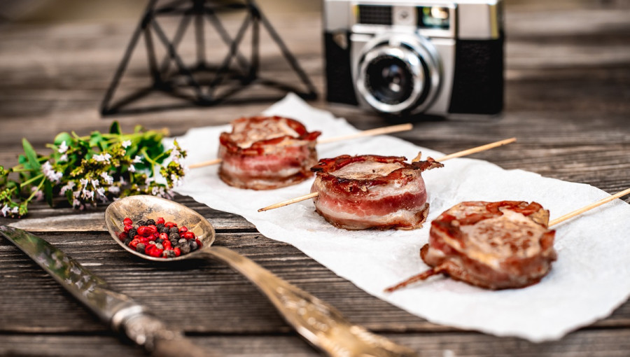 Meat on a table next to a camera and a spoon.