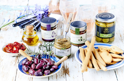 Glasses of various spreads and pickled delicacies, along with bowls of olives, dried tomatoes, and crackers.
