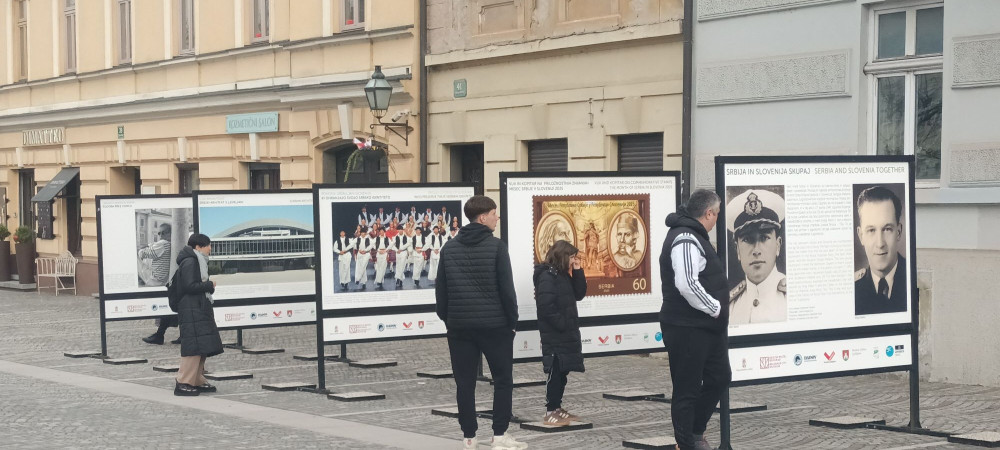 Visitors viewing outdoor exhibition panels on Gallus Embankment among historic buildings.