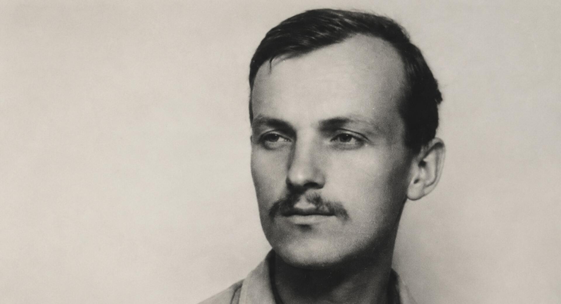 Mladenič z brado se na črnobeli fotografiji zamišljeno ozira vstran, oblečen je v svetlo srajco z ovratnikom. Ozadje je enobarvno in poudarja njegov izraz.