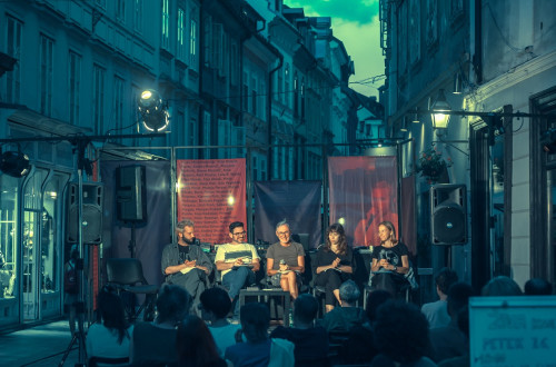 Skupina petih literatov sedi na odru, postavljenem na ulici.