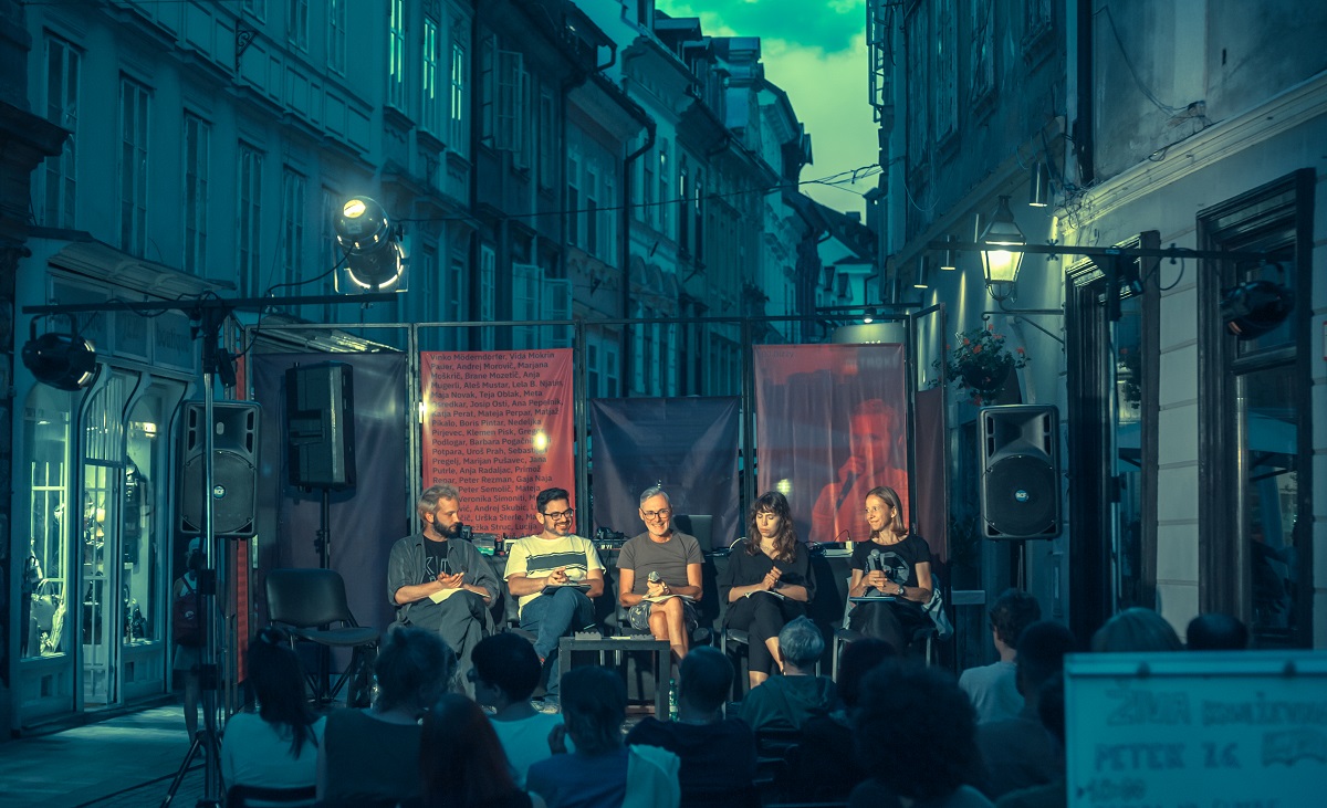 Skupina petih literatov sedi na odru, postavljenem na ulici.