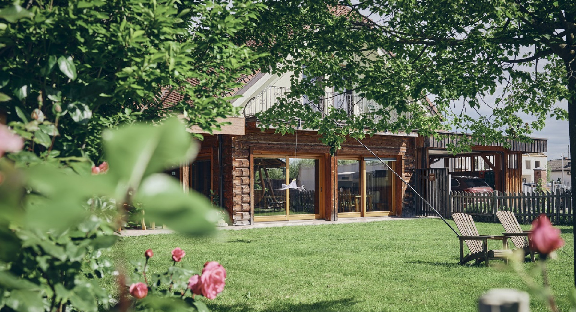 A wooden house with large glass windows in a garden with pink flowers.