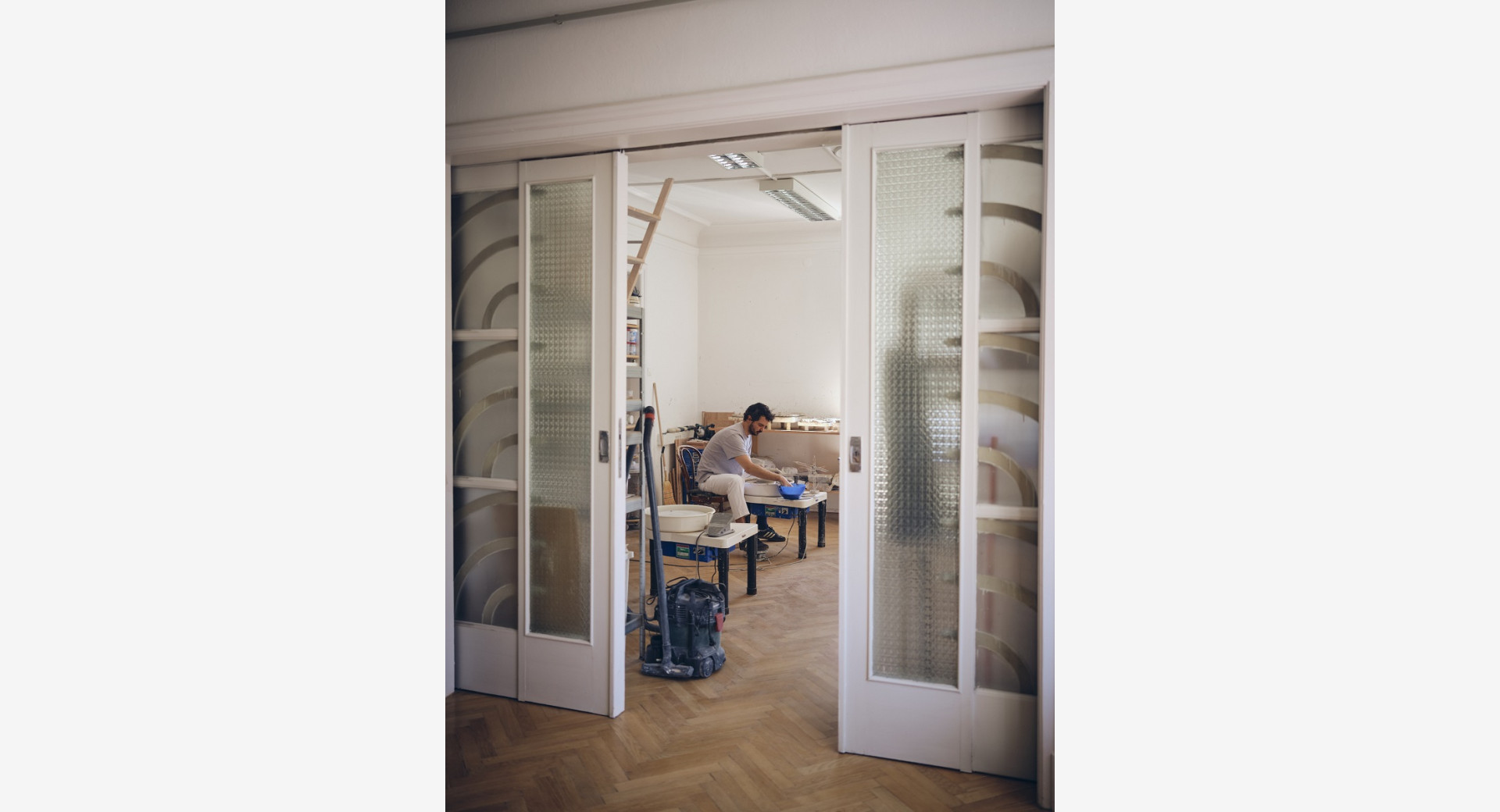 Moski, fotografiran skozi vrata, sedi za glinenim vretenom in olbikuje izdelek.