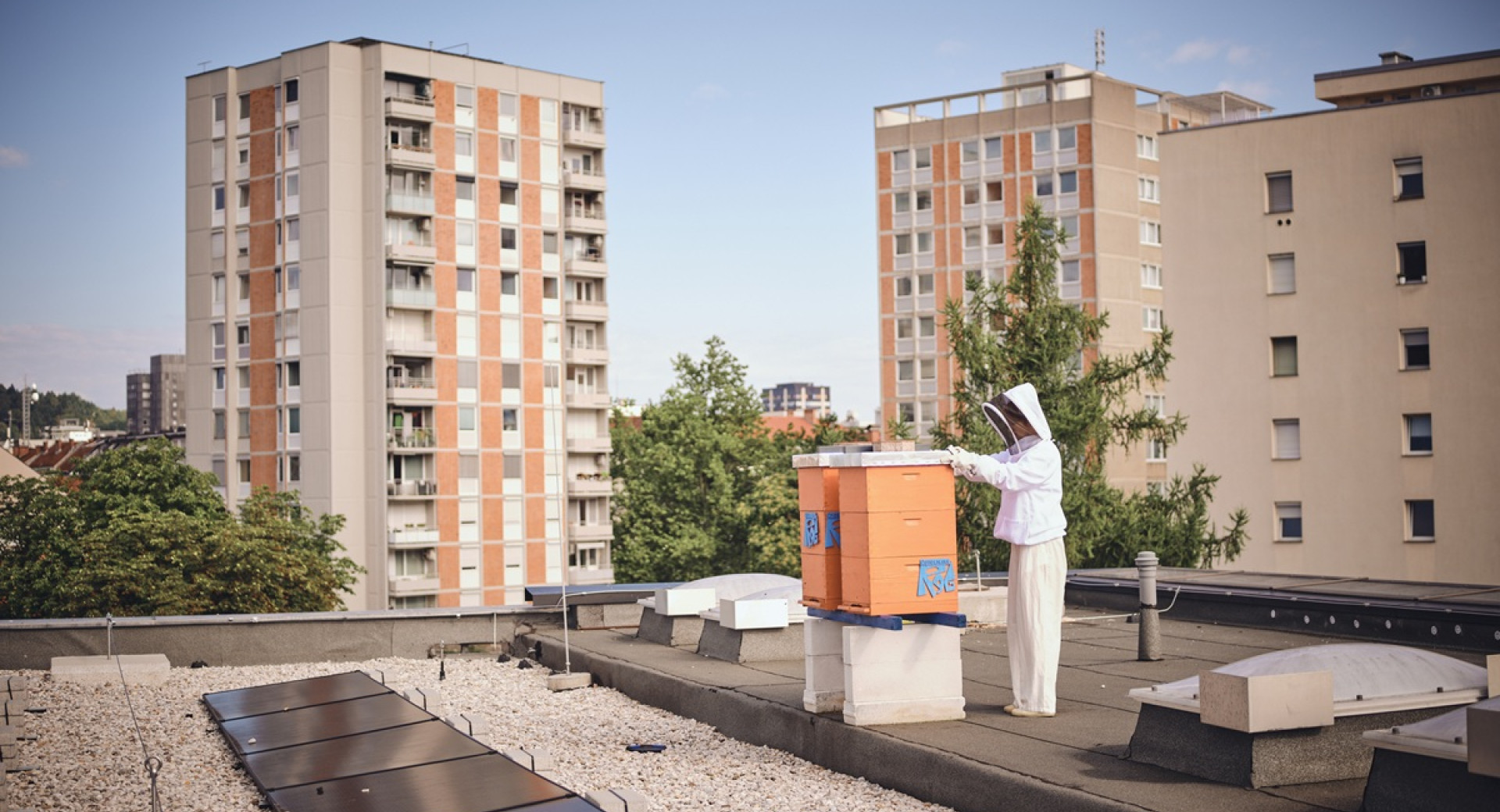 A beekeeper in a white suit on the rooftop of a building in the city.