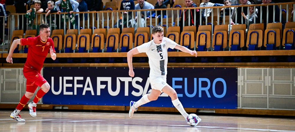 Men in red and white jerseys running after the ball in front of a packed grandstand.